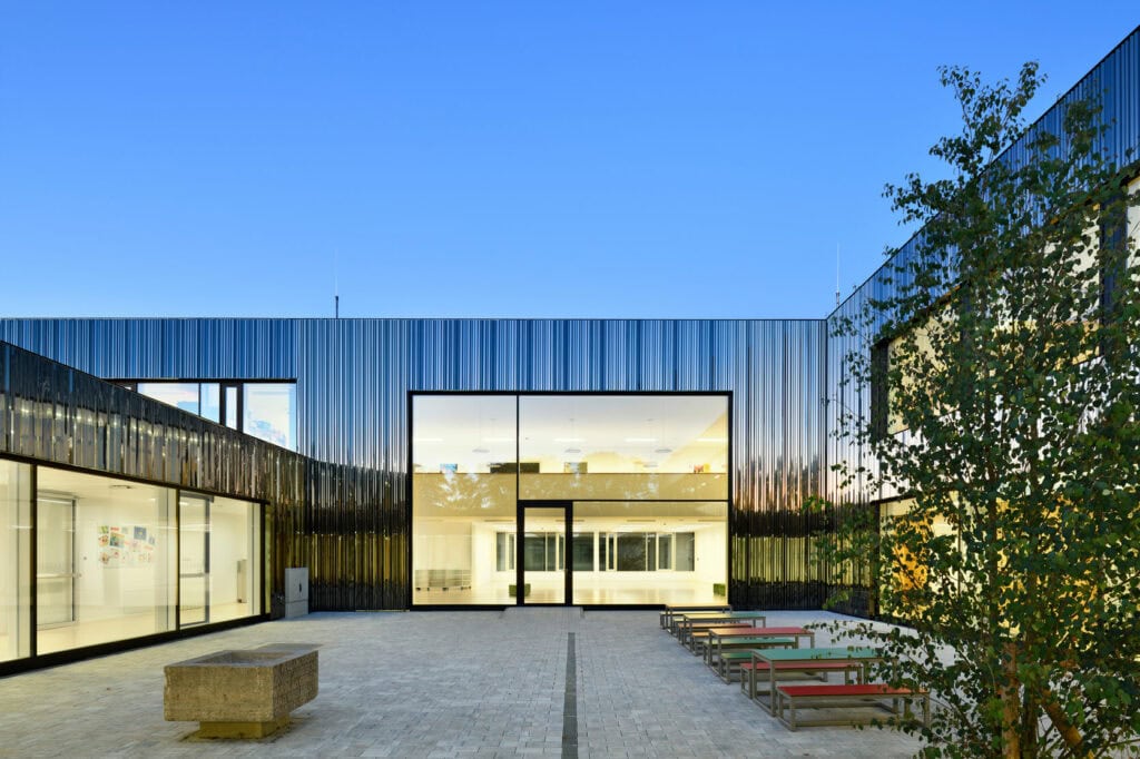 Die Fassadenverkleidung aus poliertem Edelstahlspiegel, unsichtbar befestigt an der Grundschule in Schwarzach, zudem große Fensterfronten, alles fotografiert in der blauen Stunde.