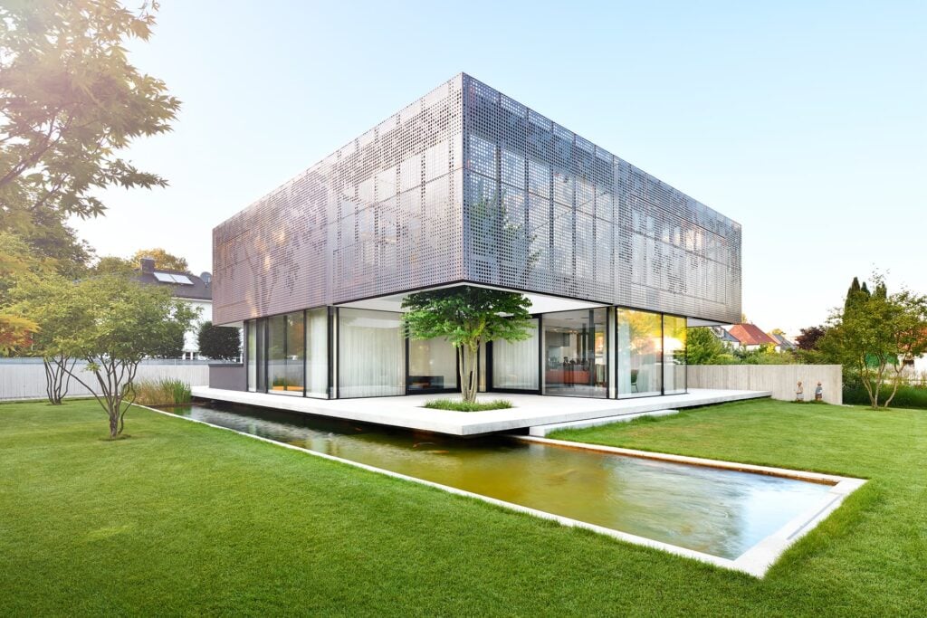 Eine moderne Villa in Niederbayern, die Fassade besteht aus gelochten Kupferkassetten, im Vordergrund ein toller Garten inklusive Koiteich.