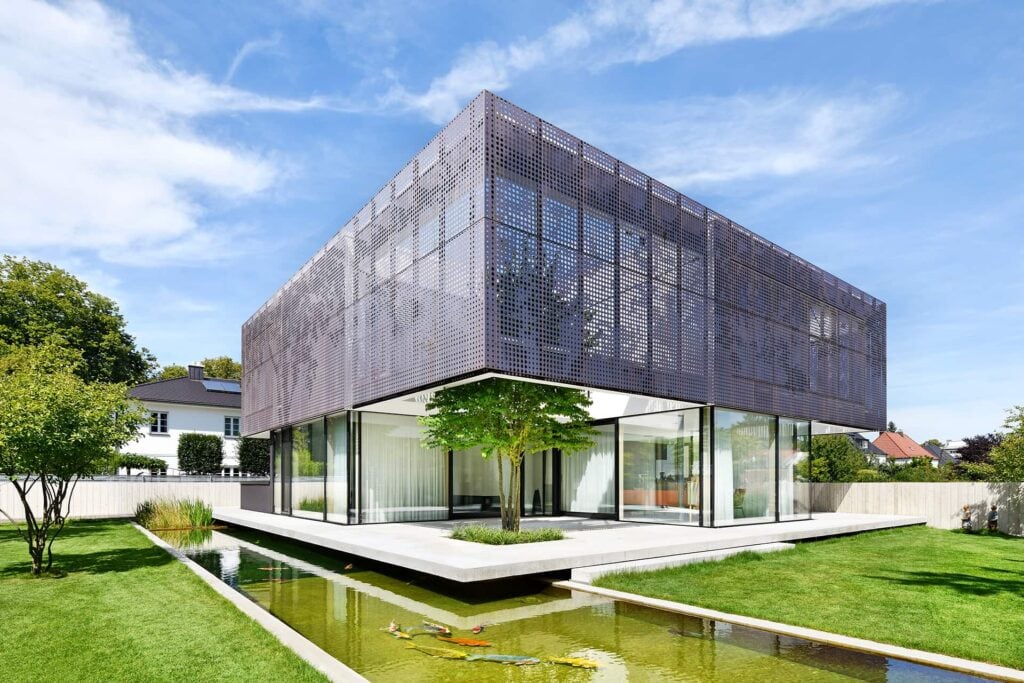 Eine moderne Villa in Niederbayern, die Fassade besteht aus gelochten Kupferkassetten, im Vordergrund ein toller Garten inklusive Koiteich